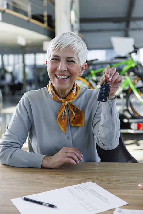 Happy senior woman holding car keys at desk