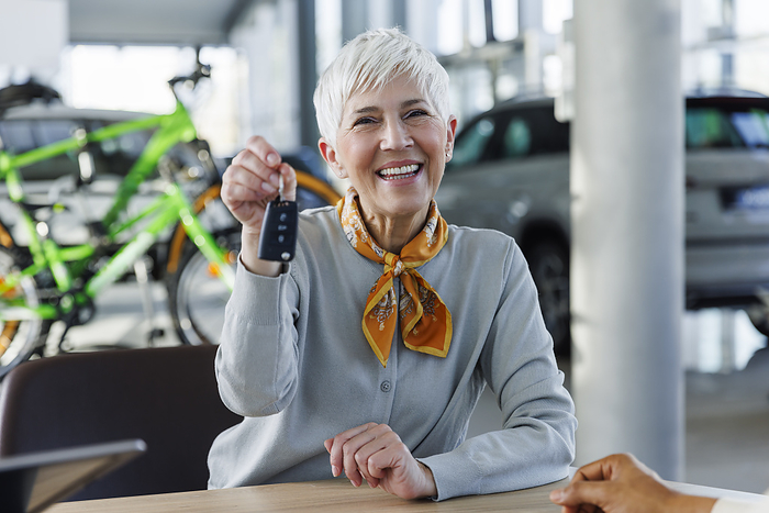 Happy senior woman holding car keys in showroom