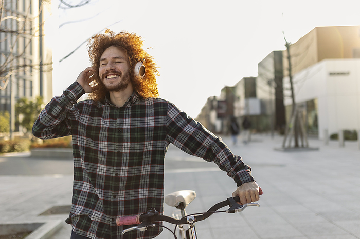 Happy man listening music through wireless headphones and walking with bicycle