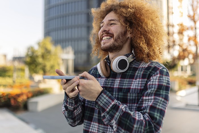 Happy curly haired man with smart phone and wireless headphones