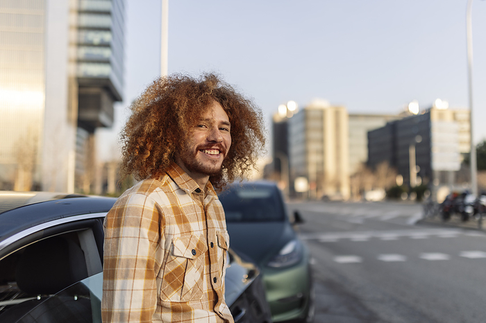 Happy curly man standing near cars on road