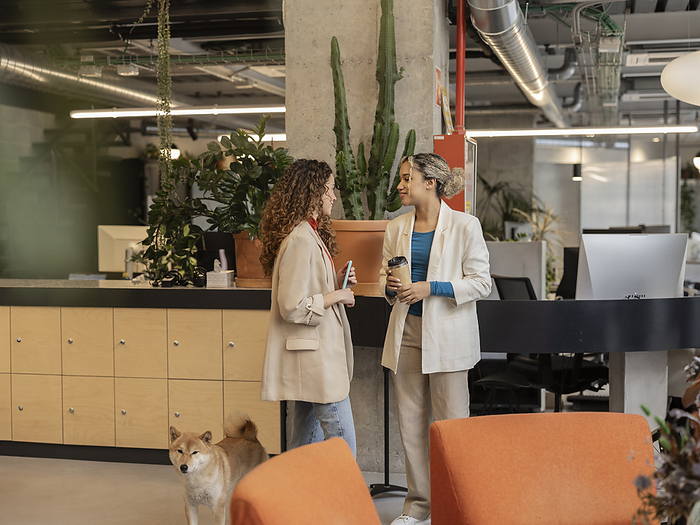 Young businesswoman discussing with colleague standing by dog at office