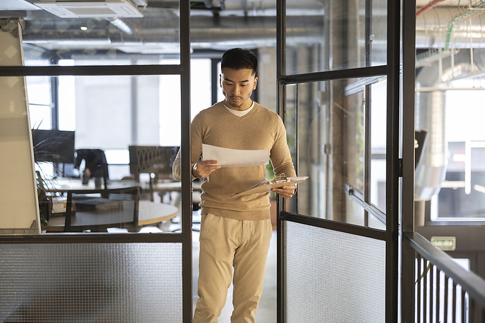 Young businessman with documents walking through door at office