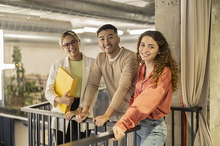 Smiling young business colleagues leaning on railing at office