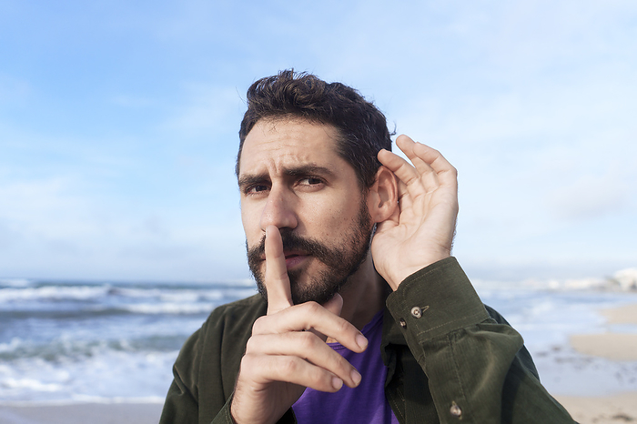 Man eavesdropping with finger on lips near sea at beach