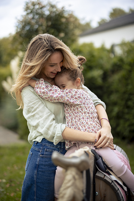 Girl sitting on wooden horse and hugging happy mother in garden