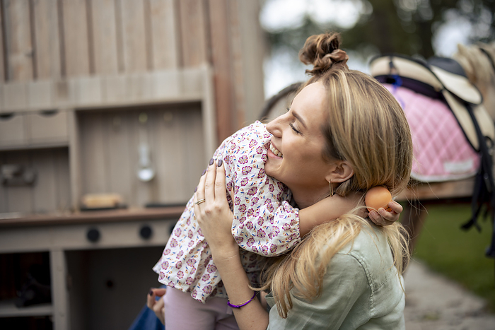 Happy mother hugging daughter near wooden horse