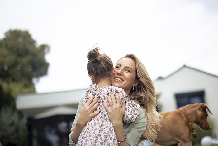 Happy woman embracing daughter near dog