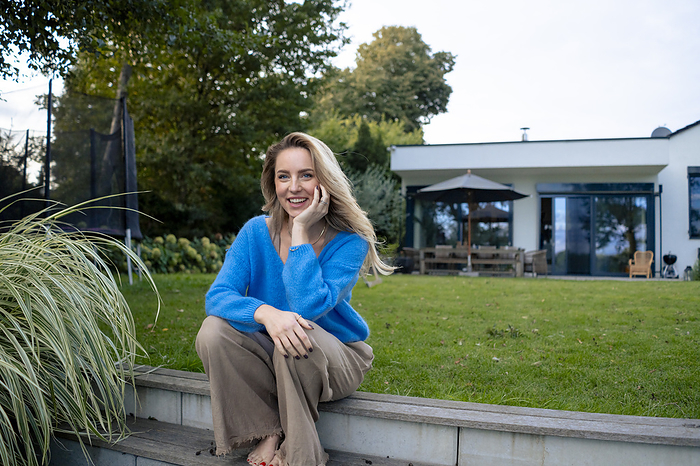 Happy blond woman sitting on steps in lawn near house