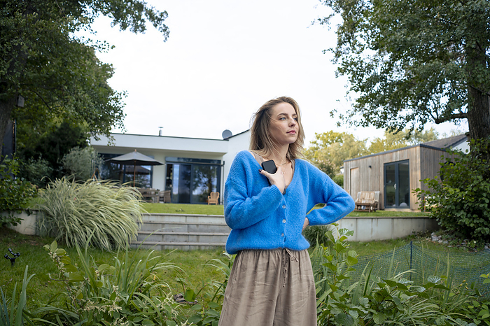 Woman standing with smart phone in front of house