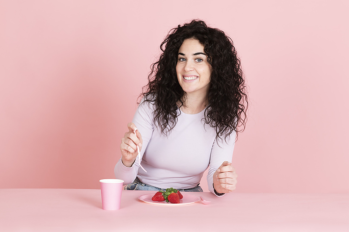 Smiling young woman with strawberries and coffee cup at table