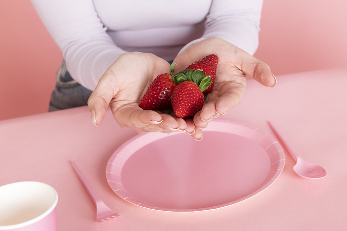 Woman holding strawberries in hand over pink empty plate
