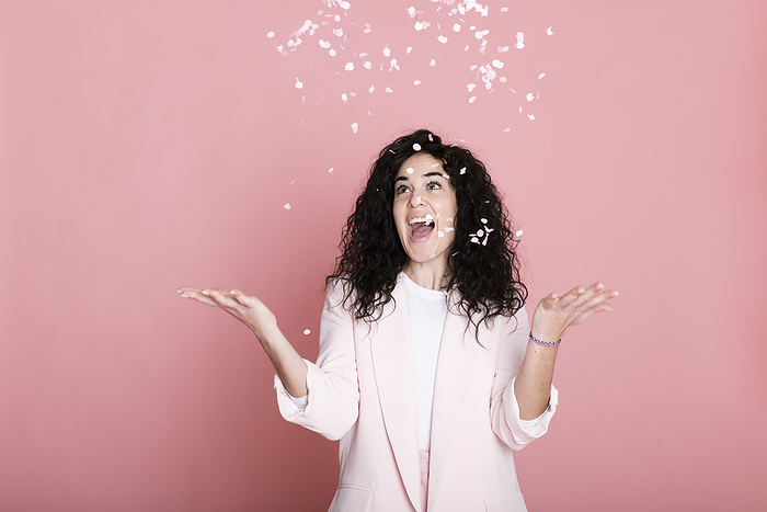 Cheerful young woman catching confetti against pink background