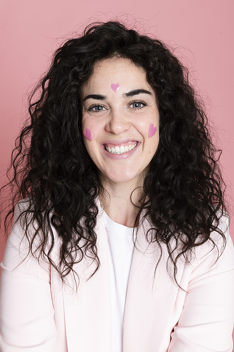 Happy woman with heart shaped stickers on face against pink background