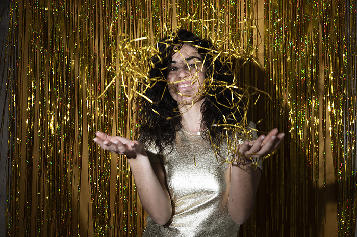 Happy woman playing with confetti in front of tinsel curtain