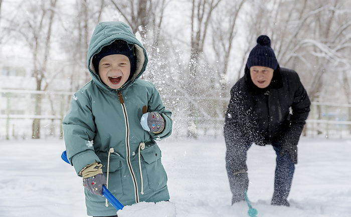 Cheerful boy playing with grandfather in snow at park