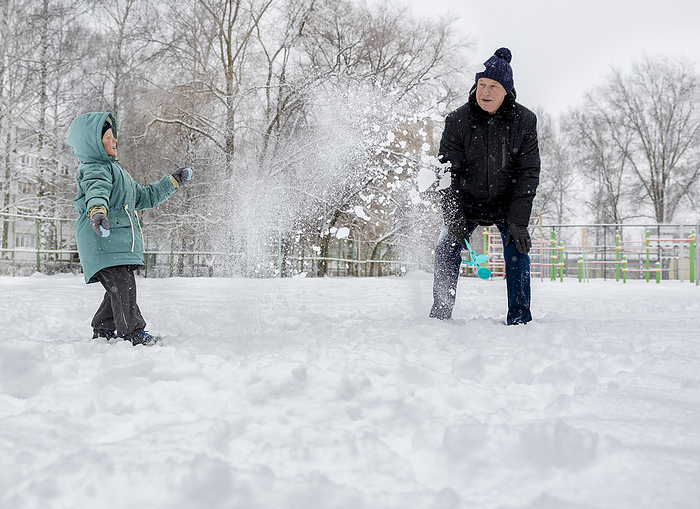 Happy boy playing with grandfather in snow at park