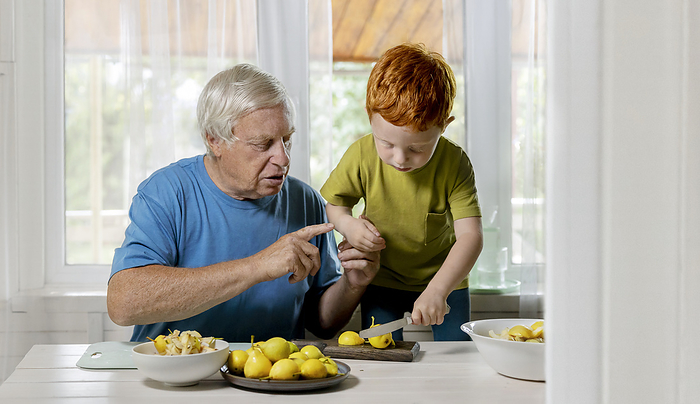 Grandfather teaching grandson to cut fruits at home