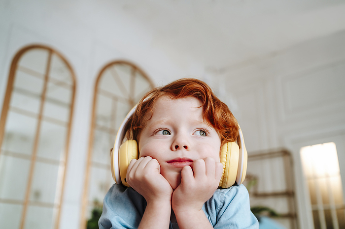 Redhead boy listening to music through wireless headphones at home