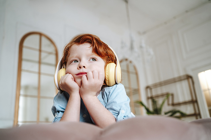 Redhead boy leaning on elbows and listening to music at home