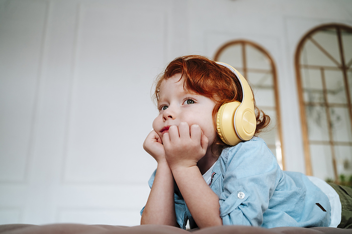 Redhead boy listening music through wireless headphones at home