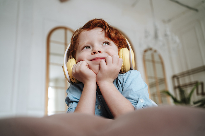 Thoughtful boy listening to music through wireless headphones at home