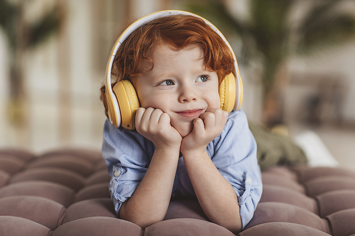 Thoughtful boy listening to music lying down on couch at home
