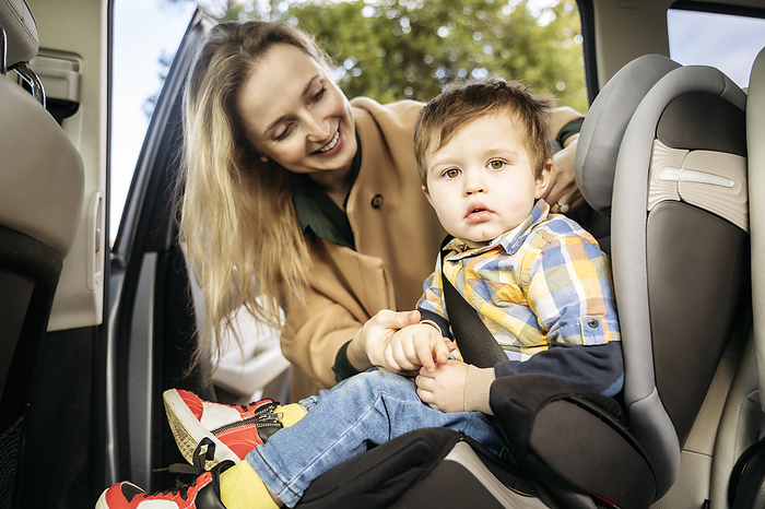 Smiling mother adjusting seat belt for son sitting in car