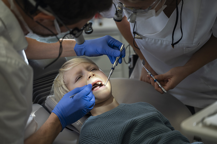 Dentist examining patient's teeth near assistant in clinic