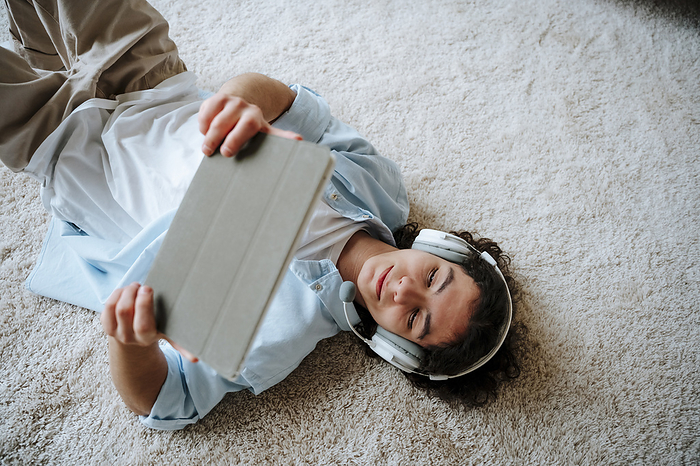 Man lying on carpet and using tablet PC at home