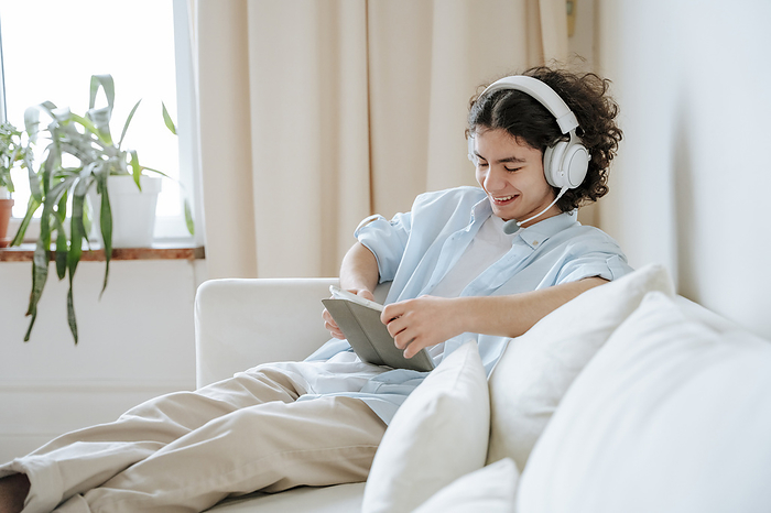 Smiling man wearing headset and using tablet PC on sofa at home