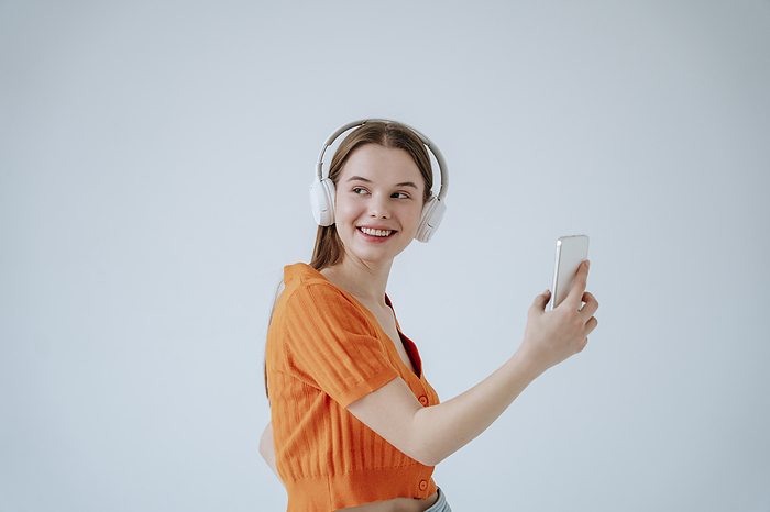 Smiling woman wearing wireless headphones and listening to music in front of white background