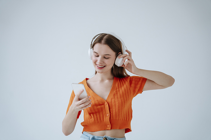Young woman wearing wireless headphones and listening to music against white background