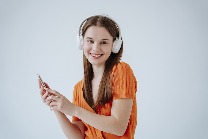 Smiling woman listening to music through wireless headphones in front of white background