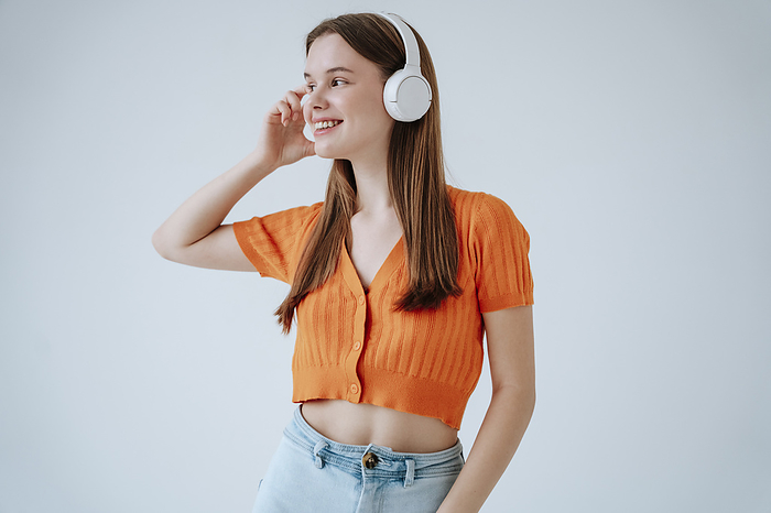 Smiling woman listening to music through wireless headphones against white background