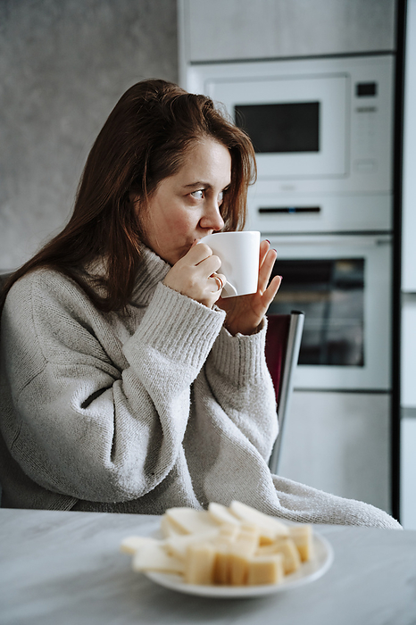 Woman drinking coffee sitting in kitchen at home