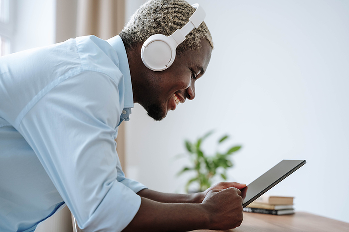 Happy man wearing wireless headphones and using tablet PC