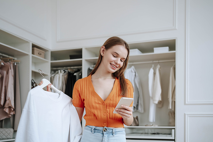 Happy woman using smart phone near closet