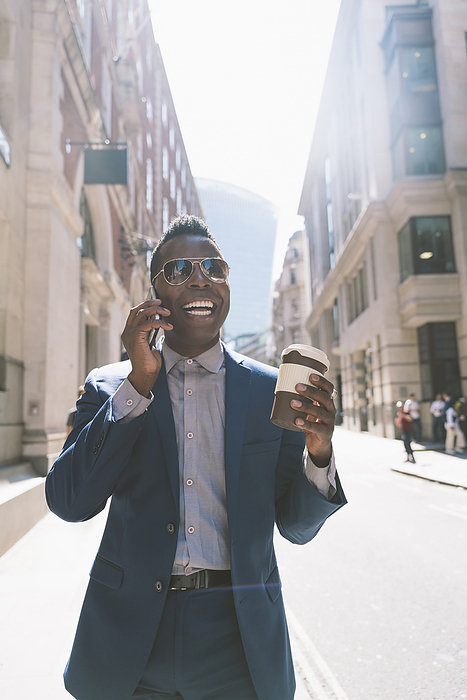 Happy businessman holding coffee cup and talking on mobile phone