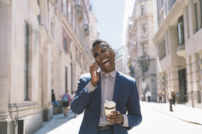 Cheerful businessman holding coffee cup and talking on smart phone