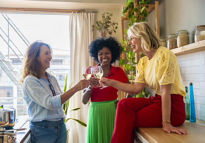 Cheerful multiracial friends toasting drinks in kitchen at home