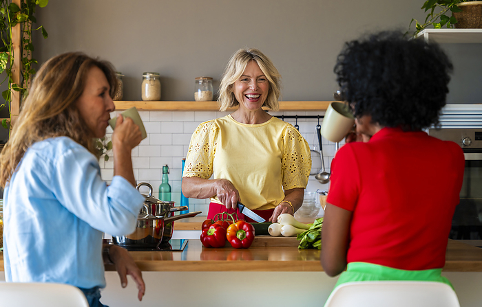 Cheerful woman cutting vegetables near friends in kitchen at home