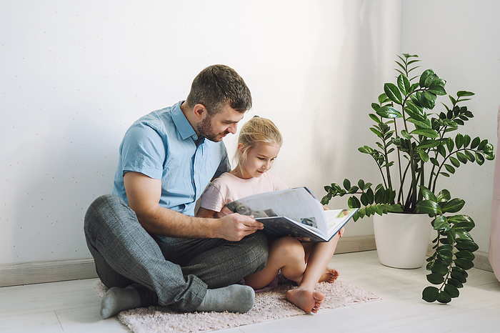 Father and daughter sitting on floor and reading book at home