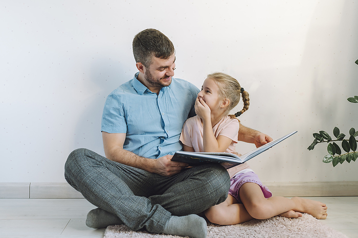 Happy father reading book to daughter in front of wall at home