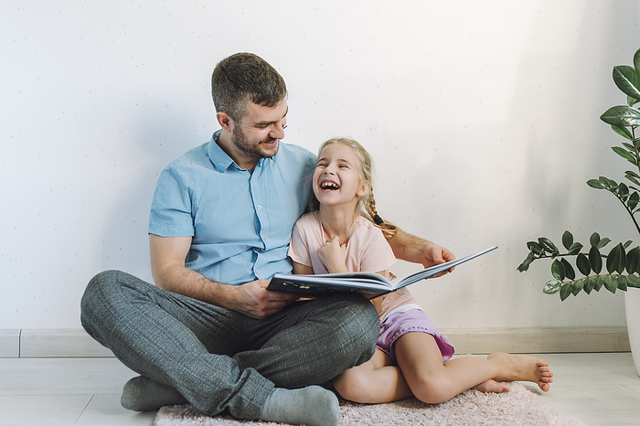 Happy man reading book to daughter in front of wall at home