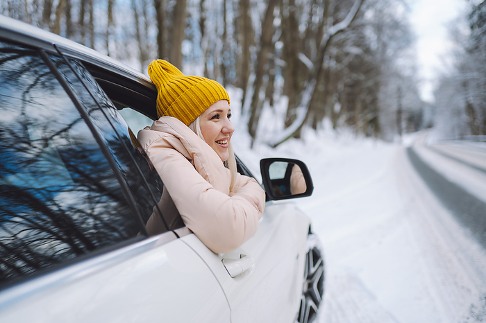 Woman wearing knit hat and leaning out of car window in winter forest