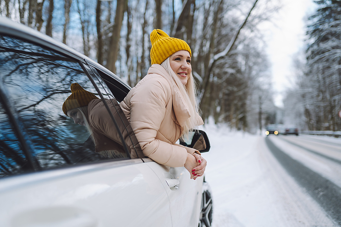 Happy woman leaning out of car window at roadside in winter forest