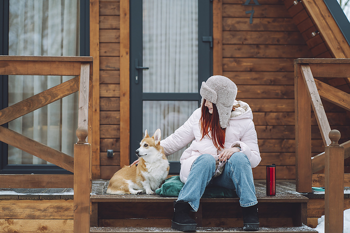 Happy woman sitting with Corgi dog on porch of log cabin