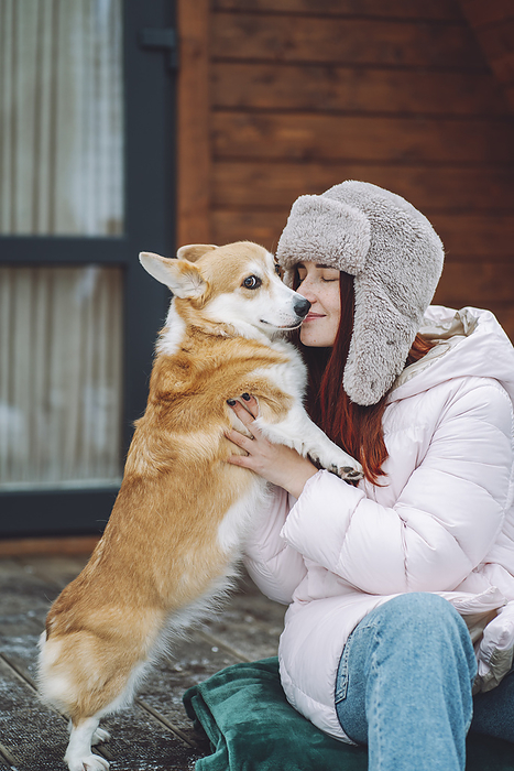 Young woman holding Corgi dog on porch