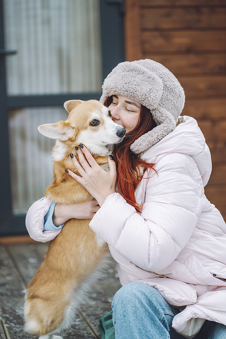 Young woman kissing Corgi dog on porch